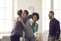 Group of colleagues hugging young man congratulating him on promotion or happy life event