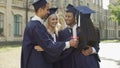 Group of college friends in academic regalia hugging together, graduation day