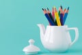 A group of color pencils in a white kettle on an backgr