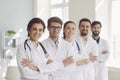 A group of confident practicing doctors in white coats are smiling against the backdrop of the clinic.