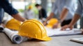 Group of construction workers in yellow hard hats review blueprints together outdoors under soft, warm light, surrounded by Royalty Free Stock Photo