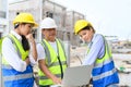 Group of contractors, engineers and formats in safety vests with helmets working with laptop, standing on under-construction Royalty Free Stock Photo