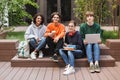 Group of cool joyful students sitting and happily looking in camera while spending time together in courtyard of