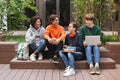 Group of cool smiling students sitting and happily looking at each other while spending time together in courtyard of