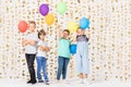 Cute teenage boys and girls is standing together in a room and holding colorful balloons Royalty Free Stock Photo