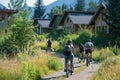 Group of cyclists enjoying a summer bike ride on a pathway surrounded by lush greenery and modern mountain lodges