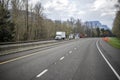 Group of different big rigs semi trucks with loaded semi trailers running on the turning wide highway road with winter bare trees