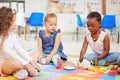 Group of diverse adorable little girls sitting cross legged on the floor in preschool and having a tea party. Three cute Royalty Free Stock Photo