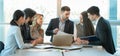 Group of diverse businesspeople going over paperwork together and working on a laptop at a table in office. Royalty Free Stock Photo