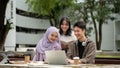 A group of diverse college students is discussing project details, using a laptop in a campus park Royalty Free Stock Photo