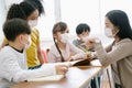 Group of Diverse Elementary School Pupils and Female Asian teacher wearing medical mask at elementary school.Teacher helping