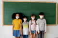 Group of diverse elementary students in classroom. Primary school pupils standing in a row wearing a face mask with