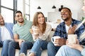 Group of diverse friends spending time togeher on weekend, holding hot drinks, having conversation and laughing at home Royalty Free Stock Photo