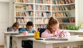 Group of diverse schoolboys and schoolgirl sitting at desks in classroom at primary school, writing in notebook Royalty Free Stock Photo