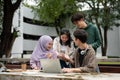 A group of diverse college students is discussing project details, using a laptop in a campus park Royalty Free Stock Photo