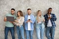 Group of diverse young friends with different gadgets studying or working together against grey studio wall Royalty Free Stock Photo