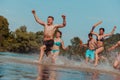 A group of diverse young people having fun together as they run along the river and play water games Royalty Free Stock Photo