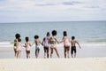 Group of eight boys and girls holding hands in a line running to sea water, cute kids having fun on sandy summer beach, happy Royalty Free Stock Photo