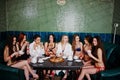 Group of eight sexy girls in swimsuits and bathrobe sitting in a bath and eating pizza. Girls rest friends Royalty Free Stock Photo
