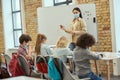 Group of elementary school kids and female teacher wearing protective mask during coronavirus pandemic writing Royalty Free Stock Photo