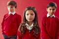 Group Of Elementary School Pupils Wearing Uniform Against Red Studio Background Royalty Free Stock Photo