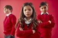 Group Of Elementary School Pupils Wearing Uniform Folding Arms Against Red Studio Background Royalty Free Stock Photo