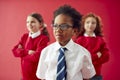 Group Of Elementary School Pupils Wearing Uniform Folding Arms Against Red Studio Background Royalty Free Stock Photo