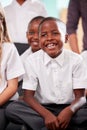 Group Of Elementary School Pupils Wearing Uniform Sitting On Floor Listening To Teacher