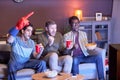 Group of emotional sports fans watching match at home lit by blue light