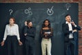 Group of employees standing by blackboard with drawn business icons, working on projects, generating ideas and fixing Royalty Free Stock Photo