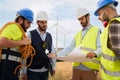 Group of engineers talking and working with a blueprint in an agricultural field with wind turbines