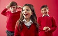 Group Of Excited Elementary School Pupils Wearing Uniform Having Fun Against Red Studio Background Royalty Free Stock Photo