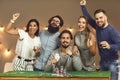 Group of excited friends celebrating successful game of poker at casino themed party Royalty Free Stock Photo