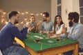 Group of excited friends with playing cards in hands sitting, betting and playing poker Royalty Free Stock Photo