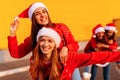 Group of excited young women wearing santa claus hats have fun and ride each other in the fresh air. New Year, celebration Royalty Free Stock Photo