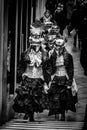 A group of females in medieval dresses and carnival masks walk at the street in Venice, Italy, black and white photo