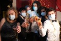 Group of fiends wearing face masks at a Christmas party looking at the camera in a bar