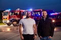 Group of firefighters, dressed in civilian clothing, stand in front of fire trucks during the night, showcasing a moment Royalty Free Stock Photo