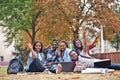 Group of five african college students spending time together on campus at university yard. Black afro friends sitting on grass