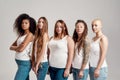 Group of five beautiful diverse young women wearing white shirt and denim jeans looking at camera while posing together Royalty Free Stock Photo