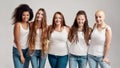 Group of five beautiful diverse young women wearing white shirt and denim jeans smiling at camera while posing together Royalty Free Stock Photo