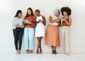 Group of five diverse young businesswomen standing against a wall in an office and using tech. Happy colleagues talking Royalty Free Stock Photo