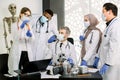 Group of five multiethnic laboratory scientists in lab coats, masks and gloves, working at lab with test tubes Royalty Free Stock Photo