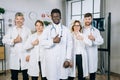 Group of five multiracial doctors in uniform standing at office room, showing thumbs up