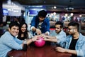 Group of five south asian peoples having rest and fun at bowling club, sitting on table and drinking soda drinks at glass bottles