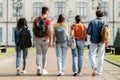 Group of five students with backpacks walking at university campus together