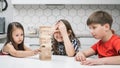 Group of focused children playing board game Jenga, building tower made of wooden blocks beams. Worried girl cover eyes.