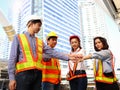 Group of four Asian man and woman engineers wear safety vest and helmet, put hands join together in downtown city, partnership