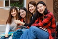 Group of four college student girls holding books, sitting and sharing time in front of outside school building with happy and fun Royalty Free Stock Photo