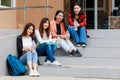 Group of four college student girls holding books, sitting and sharing time in front of outside school building with happy and fun Royalty Free Stock Photo